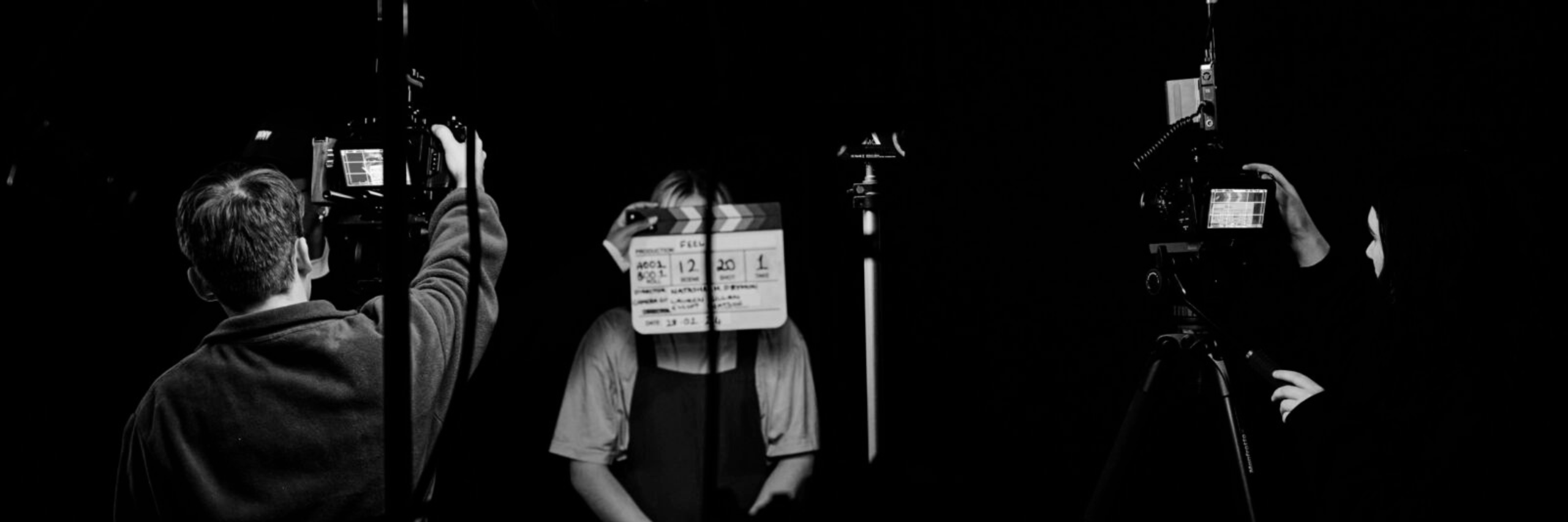 black and white image two hold cameras one sits infront of them