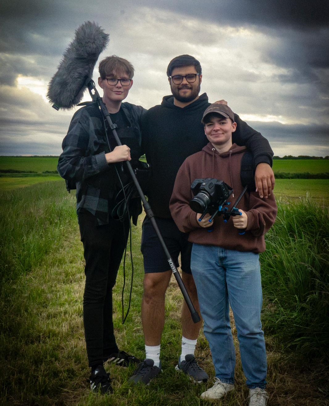 three crew members pose in the fields of a film set with equipment